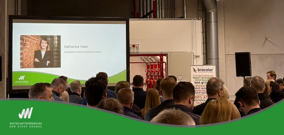 Vortragssituation bei einer Veranstaltung mit Publikum. Auf einer großen Leinwand ist eine Präsentationsfolie mit dem Namen „Katharina Vater“ zu sehen. Die Zuhörenden sitzen vor der Bühne in einer Halle oder einem Veranstaltungsraum.
